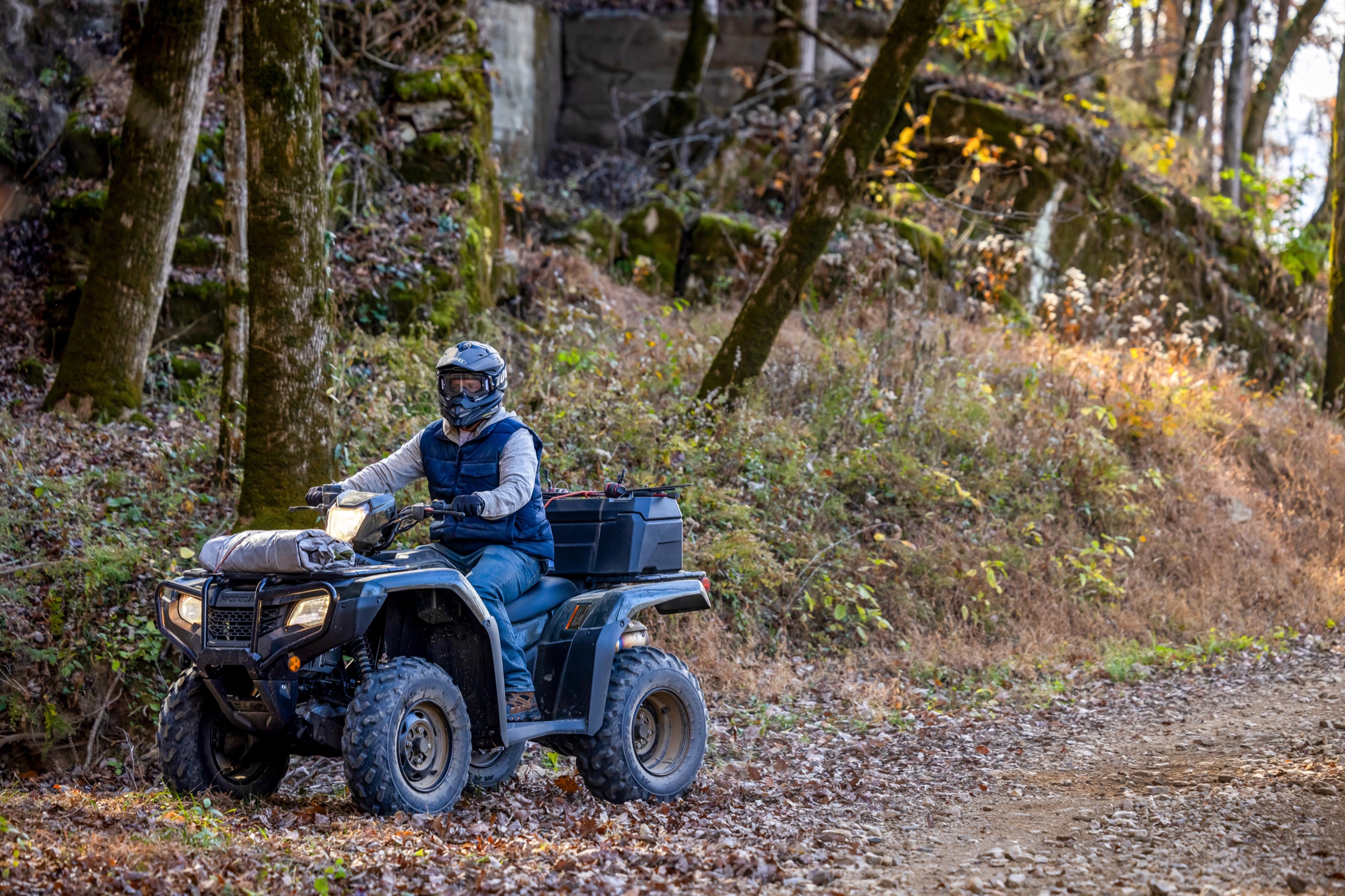 Helmeted rider on a Honda Foreman ATV along a wooded trail