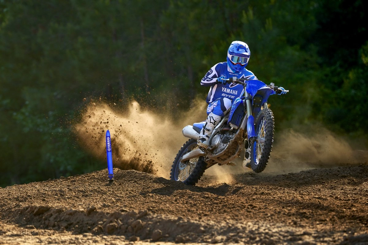 Helmeted rider on a blue Yamaha YZ250F on a dirt track.