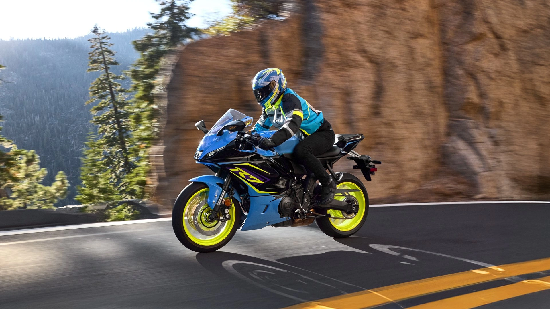 Helmeted rider on a blue 2026 Yamaha YZF-R7 riding a paved mountain road.